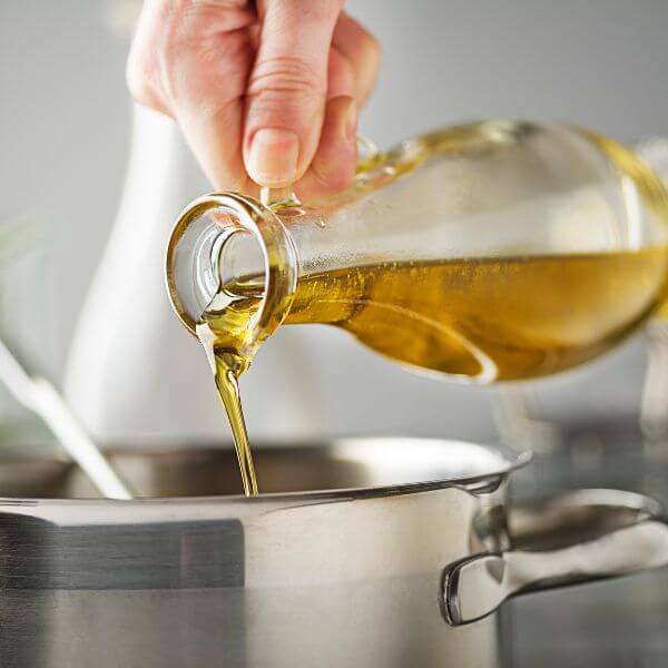 A stream of olive oil being poured from a glass bottle into a stainless steel pot during cooking.
