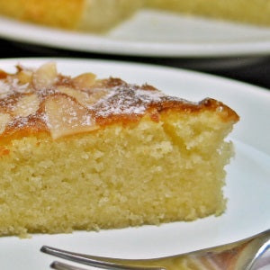 A slice of almond-topped lemon almond cake dusted with powdered sugar and served on a white dessert plate.