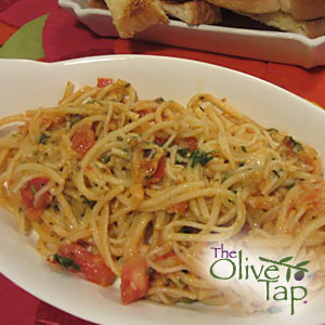 Angel hair noodles tossed with diced tomatoes, olives, fresh herbs, and a light sauce, served in a white bowl with slices of bread in the background.