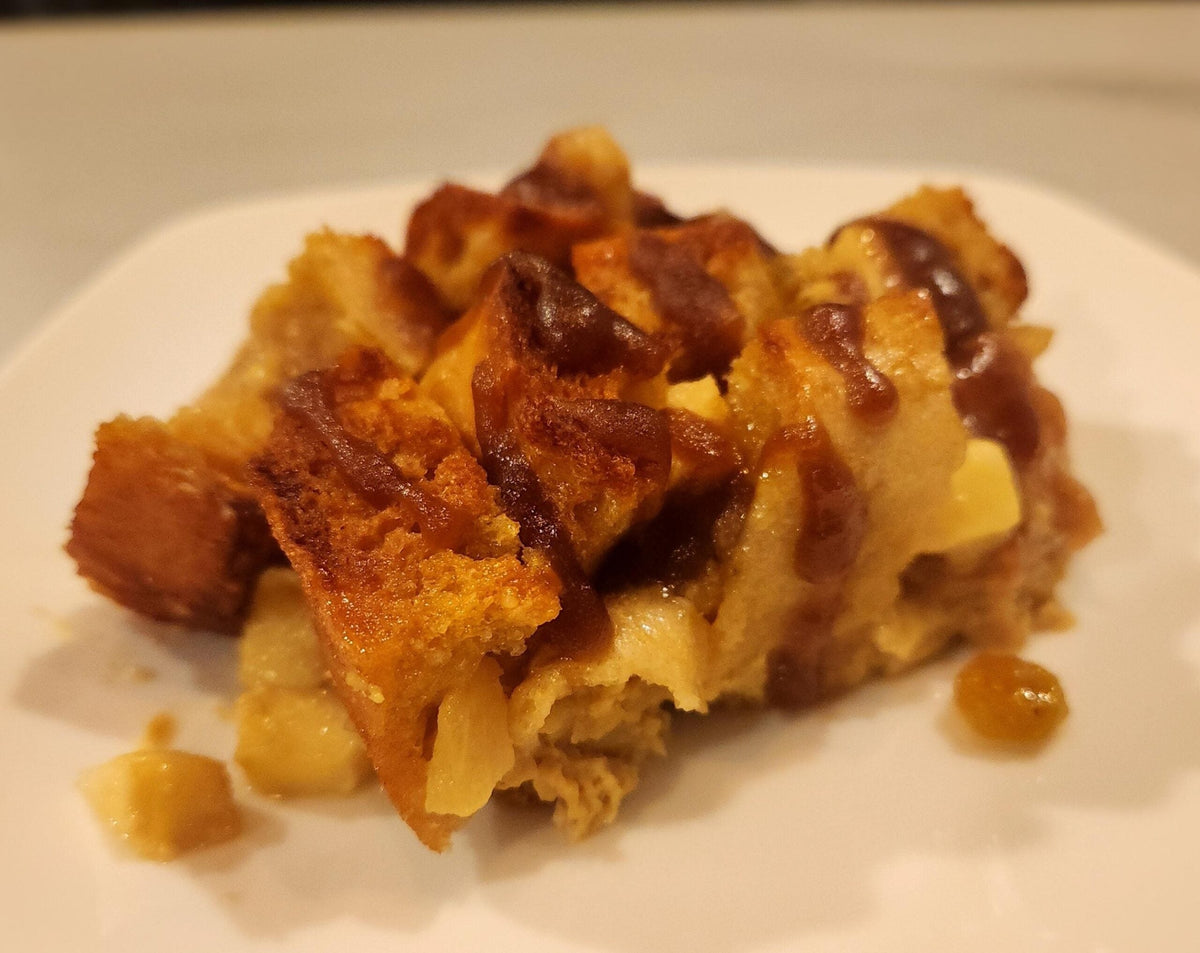 Bread cubes topped with apples and drizzled with caramel as a bread pudding on a white plate.