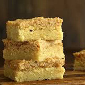 Stack of apple butter cake squares with a golden crumb topping, arranged on a wooden surface.