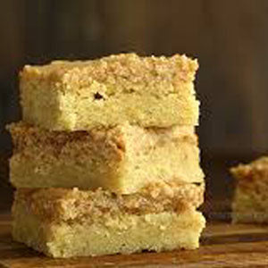 Stack of apple butter cake squares with a golden crumb topping, arranged on a wooden surface.