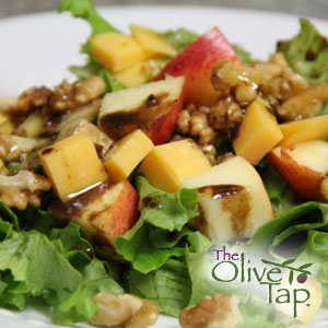 Fresh holiday salad made with mixed greens, sliced apples, cubed cheese, walnuts, and balsamic dressing, served on a white plate.