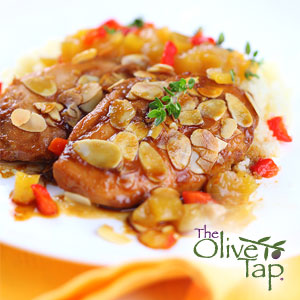 Chicken breasts topped with toasted almonds and a savory sauce, served on a white plate with rice and diced peppers, garnished with fresh herbs.