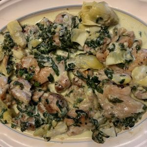 Creamy artichoke chicken with spinach and artichoke hearts served on a white plate.
