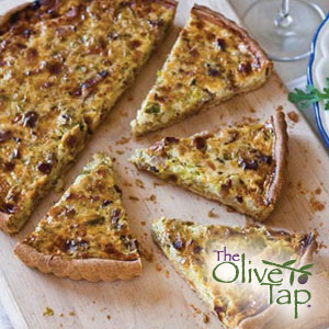 A quiche with bacon, artichokes, and parmesan sliced and on a wooden cutting board.