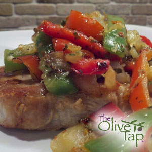Pork chop topped with mixture of pineapple, bell peppers, and onions, served on a white plate.