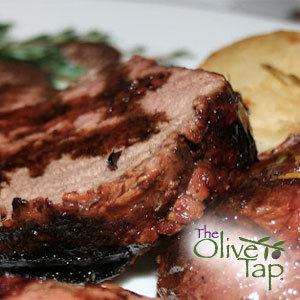 Slice of roasted pork topped with a rich balsamic cranberry wine sauce, served on a white plate with a golden potato side dish.
