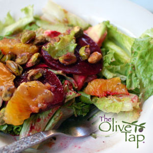 Leafy greens topped with oranges, beets, and pistachios, served on a white plate.