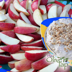 Sliced red apples served with a cream cheese dip topped with chopped nuts in a colorful bowl.