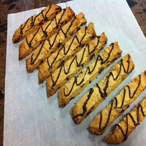 A row of chocolate chip biscotti drizzled with chocolate sauce on parchment paper.