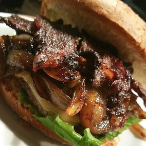 A bison burger topped with lettuce, cheese, grilled onions, and thick cut, glazed bacon, served on a bun.