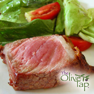 A slice of seasoned steak on a white plate with a side salad of lettuce and sliced tomato with a dressing.