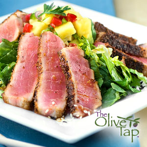 Seared, seasoned tuna on a bed of greens and topped with a mango salsa served on a white plate.