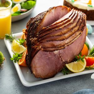Bourbon maple balsamic glazed ham sliced and served on a white platter, garnished with citrus wedges and fresh herbs.