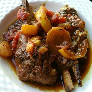 Braised lamb shoulder with yellow squash and tomatoes served in a white bowl with cooking juices.