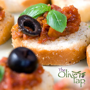 Bread slices topped with bruschetta and a slice of black olive and garnished with basil.