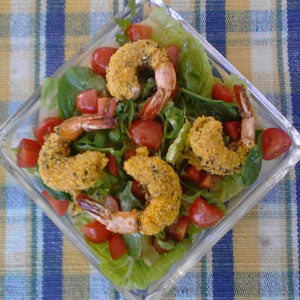 Leafy green salad topped with tomatoes and herb-crusted shrimp, served in a glass bowl on a plaid tablecloth.