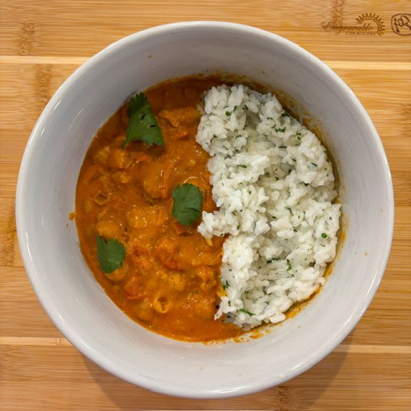 A bowl of chickpea tikka masala topped halfway with mashed cauliflower and cilantro in a white bowl on a wooden surface.