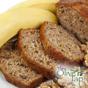 Sliced loaf of banana bread next to bananas and walnut pieces.