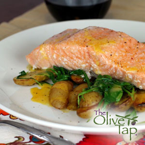 Baked salmon fillet served over sautéed greens and roasted baby potatoes, finished with a glaze and presented on a white plate.
