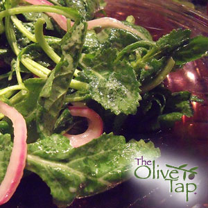 Fresh leafy green salad with sliced, pickled red onions and tender greens lightly dressed and served in a dark bowl.