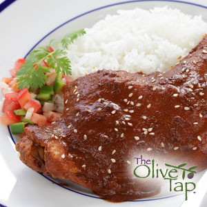Chicken with a mole sauce and sesame seeds, served with rice and fresh salsa, served in a white bowl.
