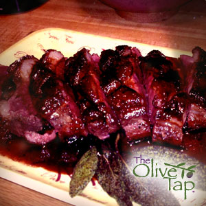 Sliced duck breast with a cherry balsamic sauce served on a platter with fresh herbs.