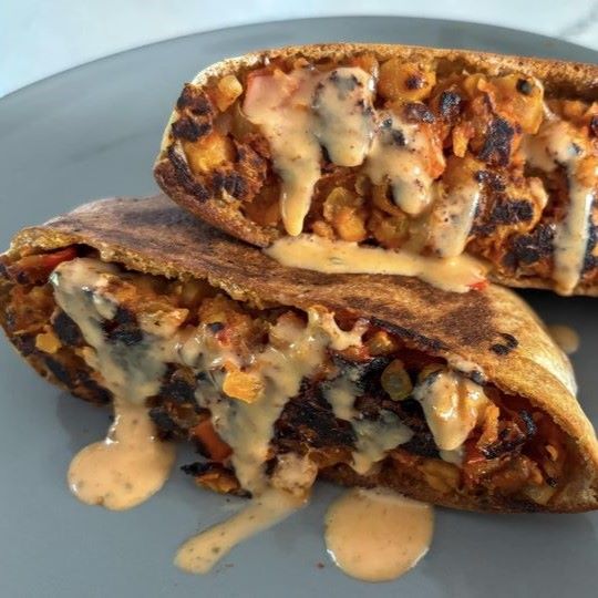 Two pita pockets stuffed with a chickpea filling, drizzled with a creamy sauce and served on a gray plate.