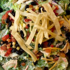 Leafy green salad topped with black beans, corn, tomatoes, shredded chicken, and topped with tortilla strips.