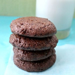 A stack of chocolate balsamic fudge cookies on a blue surface with a glass of milk in the background 