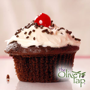 Chocolate cupcake topped with fresh whipped cream, chocolate sprinkles, and a cherry on top.