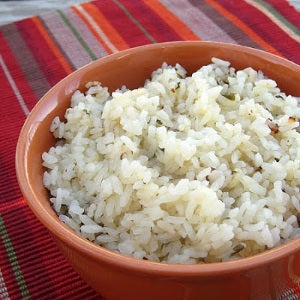 A bowl of cumin lime rice flecked with herbs, served in a terracotta dish.