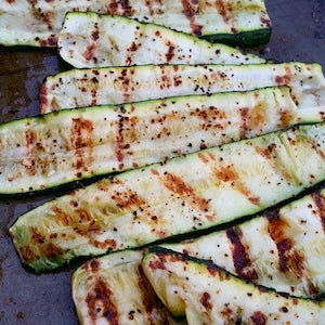 Grilled zucchini slices with charred grill marks and seasoning served on a cooking surface.