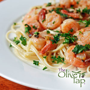 A white plate of noodles topped with whole shrimp and garnished with chopped fresh parsley.