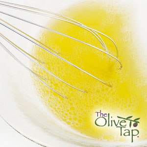 A close up of a yellow vinaigrette in a glass bowl with a whisk.