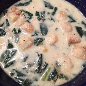 A bowl of creamy chicken soup with spinach, leeks, and diced chicken in a light broth and topped with croutons.