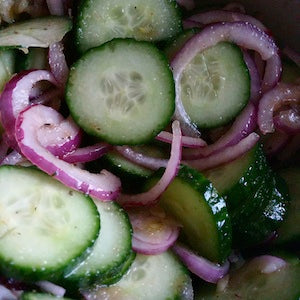 A close-up of a sliced cucumber and red onion salad, coated in a vinaigrette.