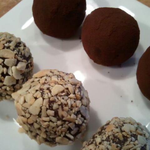 Dark chocolate truffles coated in cocoa powder and chopped nuts, arranged on a white plate.