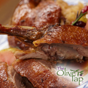 Sliced roasted duck with crispy skin served on a platter with pan sauce and fruit garnish.