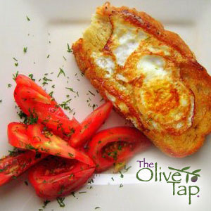 Egg-in-a-hole toast featuring a fried egg cooked inside a slice of golden toasted bread, served with fresh tomato wedges and sprinkled with herbs on a white plate.