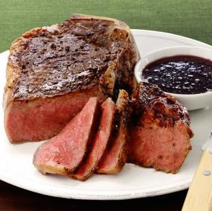 Thick-cut grilled steak with slices revealing medium-rare center, served with a sherry vinegar steak sauce, served on a white plate.