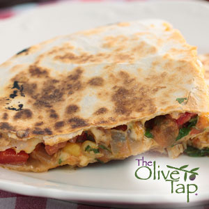 A quarter of a quesadilla on a white plate stuffed with goat cheese, red peppers, onion, green olives, and fresh basil.