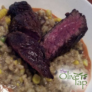 Sliced medium-rare steak served over risotto, presented in a white bowl.