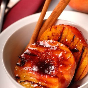 Grilled peach halves drizzled with raspberry balsamic glaze and served in a white bowl with cinnamon sticks.