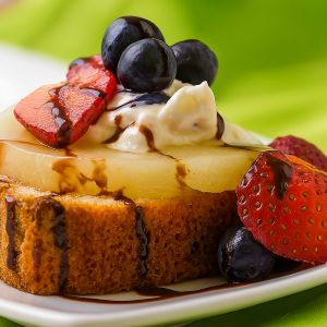 A slice of grilled pound cake topped with a pineapple ring, strawberries, blueberries, and whipped cream, drizzled with dark chocolate balsamic vinegar.