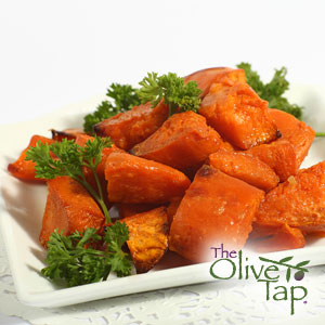 Grilled cubes of sweet potato served on a white dish and garnished with curly parsley on a white surface.