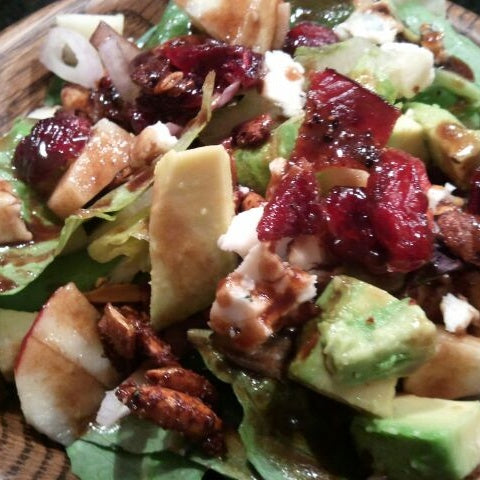 Salad topped with cheese cubes, avocado, balsamic glazed bacon, dried cranberries, and seasoned pepitas, drizzled with a balsamic vinegar.