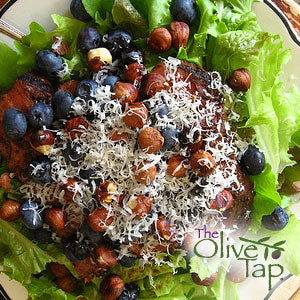 A bed of leafy greens topped with blueberries, hazelnuts, and goat cheese served on a white plate.