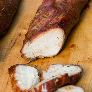 Sliced, smoked pork tenderloin on a wooden cutting board.
